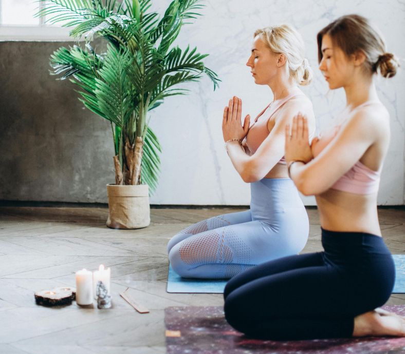 Two women meditate in a tranquil yoga studio setting, enhancing mindfulness and relaxation.